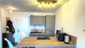 Une cuisine moderne avec des meubles gris, un plan de travail en bois, un évier, une bouilloire et une chaise.