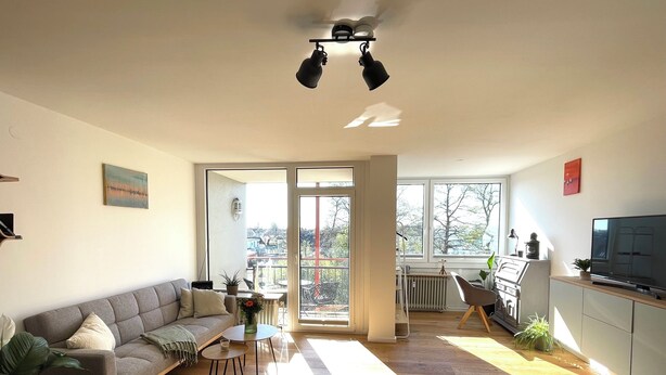 Un salon moderne avec un canapé gris, une petite table ronde et un téléviseur posé sur un meuble.