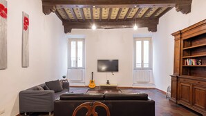 Ein Wohnzimmer mit einer Couch, einem Esstisch, einer Gitarre und einem Fernseher.