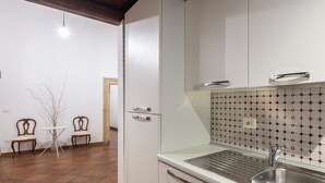 Eine Küche mit weißen Schränken, einer Edelstahl-Spüle und einer gefliesten Rückwand. Im Hintergrund steht ein kleiner Tisch mit Stühlen.