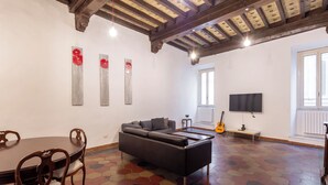 Ein Wohnzimmer mit einer Couch, einem Esstisch mit Stühlen, einem Fernseher und Bildern an der Wand.