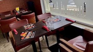 En restaurang med träbord och röda läderstolar, en meny på bordet och utsikt över en moské genom ett fönster.