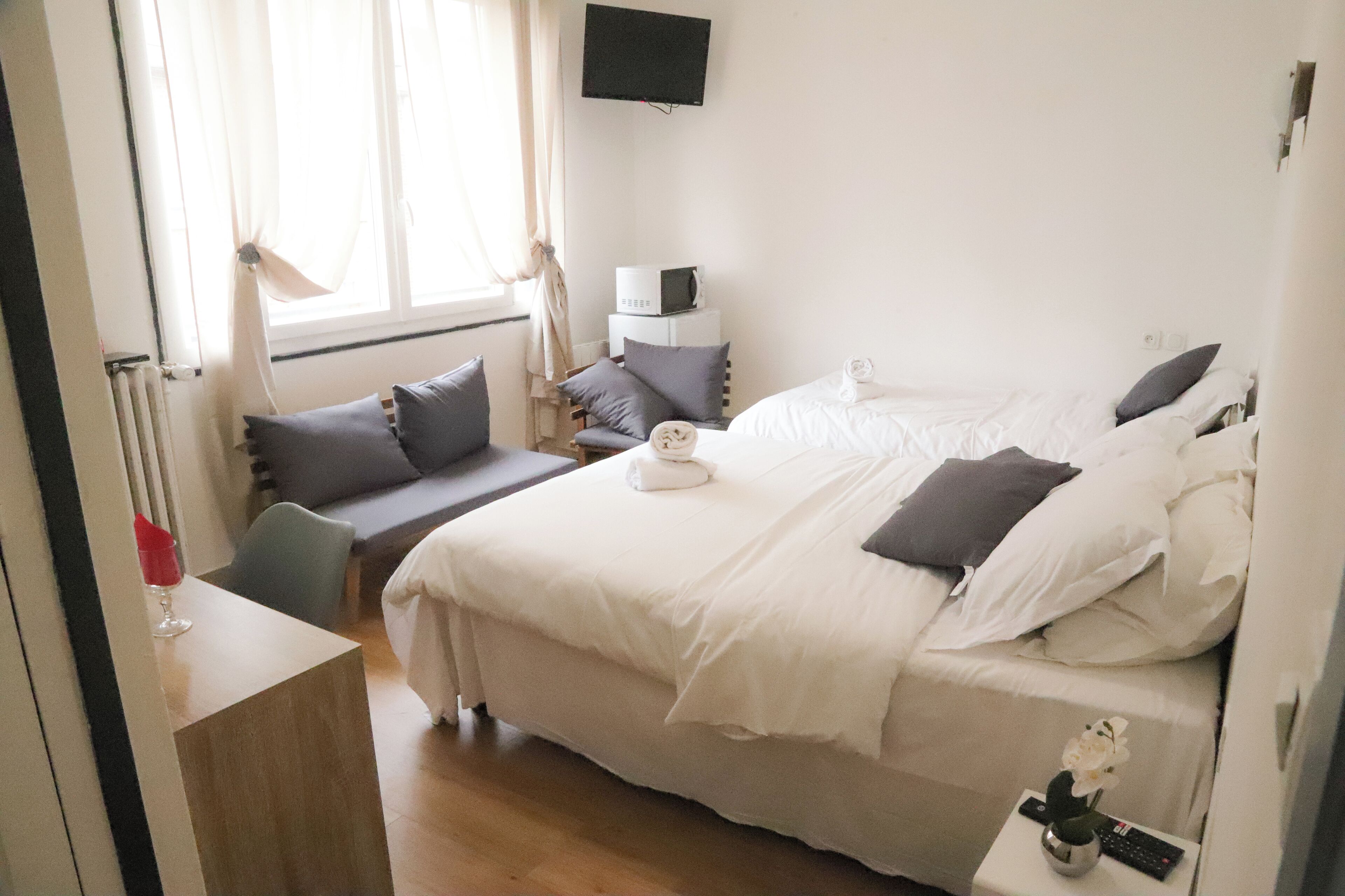 Habitación de hotel con cama, un escritorio pequeño, una silla, un televisor montado en la pared y una ventana con cortinas.