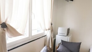 Ett rum med en soffa och två fåtöljer, en tv som är monterad på väggen och en liten vit apparat på ett bord.