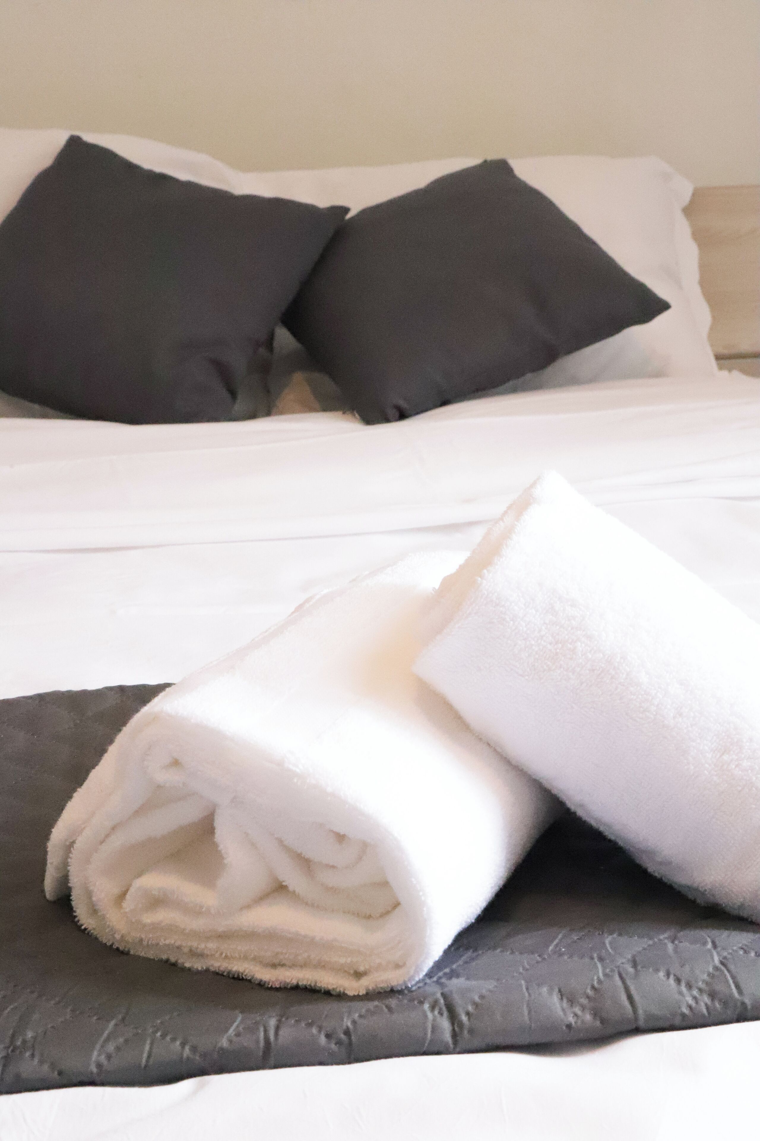 A neatly made bed with white linens and two dark pillows.