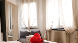 En snyggt bäddad säng med ett vitt täcke och en brun överkast, en röd, mjuk leksak och en vas med blommor på nattduksbordet.
