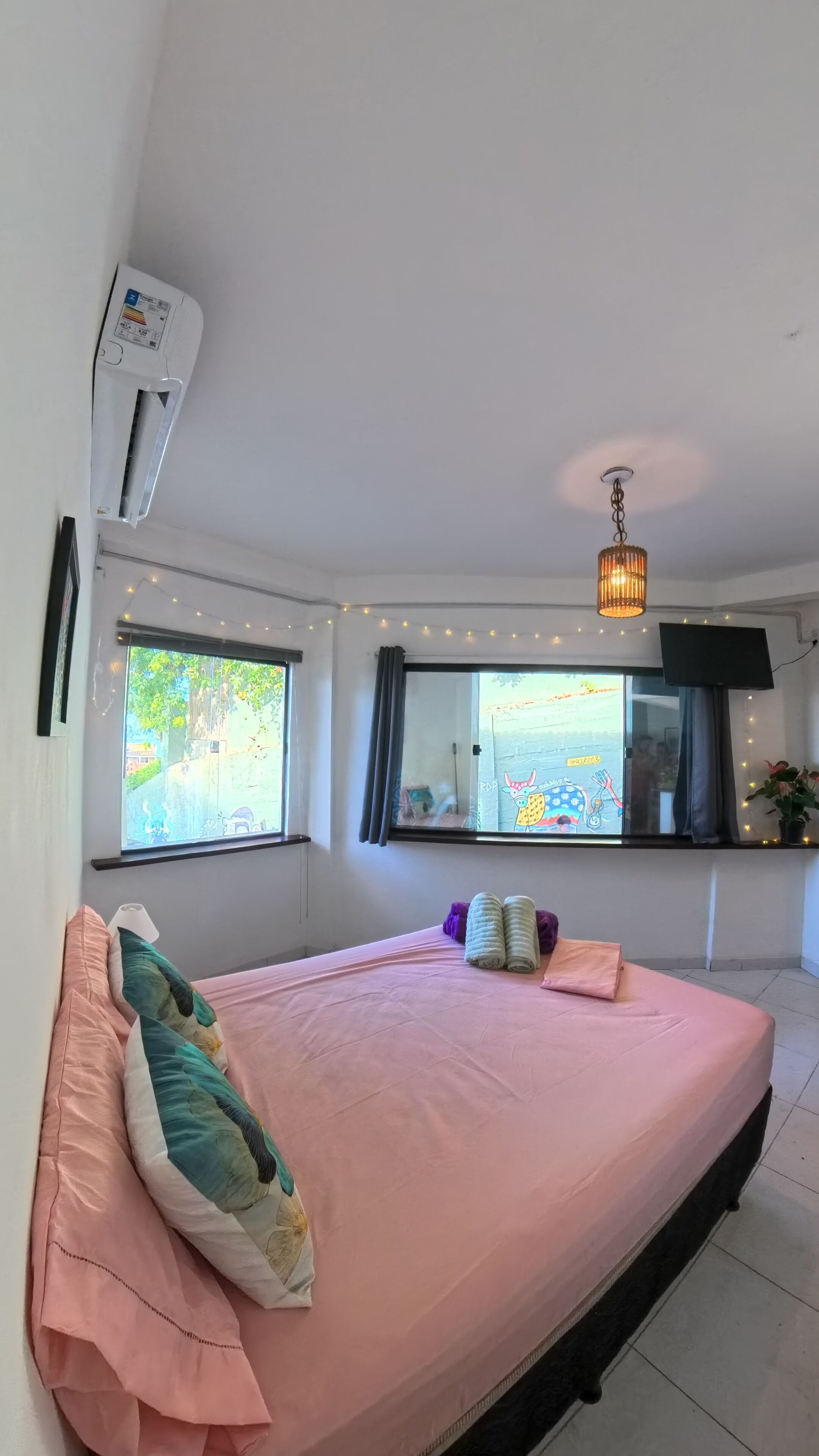 Un dormitorio con una cama, dos ventanas, un televisor y una lámpara en el techo.