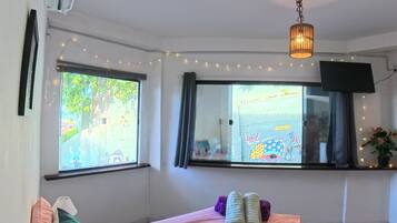 Un dormitorio con una cama, dos ventanas, un televisor y una lámpara en el techo.