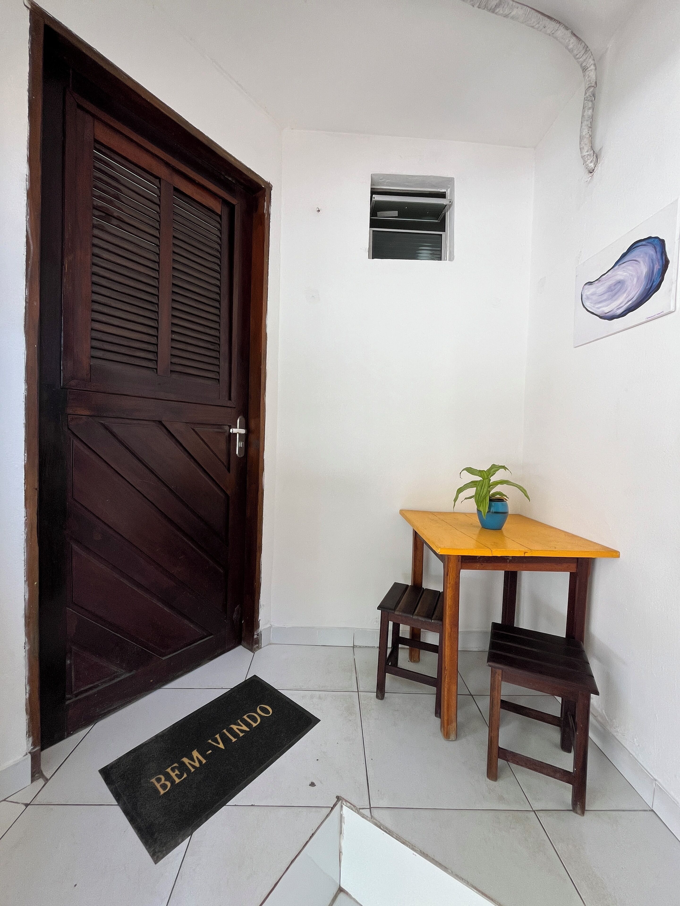 A room with a wooden door, a small table with a potted plant, a doormat, and a wall-mounted air conditioning unit.