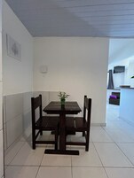 A dining area with a wooden table and chairs, a potted plant, and a kitchen in the background.