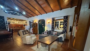 A cozy living room with a sofa, armchair, and coffee table, a dining area with a table and chairs, and a kitchen in the background. - Casa Vimeiro Sleeps 2 With Pets (Alcobaça)