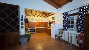 A spacious kitchen with wooden beams, a wine rack, and a dining area with a chair and table. - Casa Vimeiro Sleeps 2 With Pets (Alcobaça)