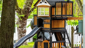 A wooden playhouse with a slide, surrounded by trees and greenery.