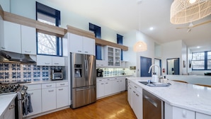 A modern kitchen with white cabinets, a stainless steel refrigerator, a built-in oven, and a wooden floor.