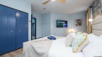A bedroom with a bed, a ceiling fan, a TV on the wall, and a blue wardrobe.