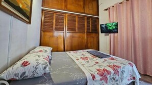 A bedroom with a wooden wardrobe, a television, and floral bedding.