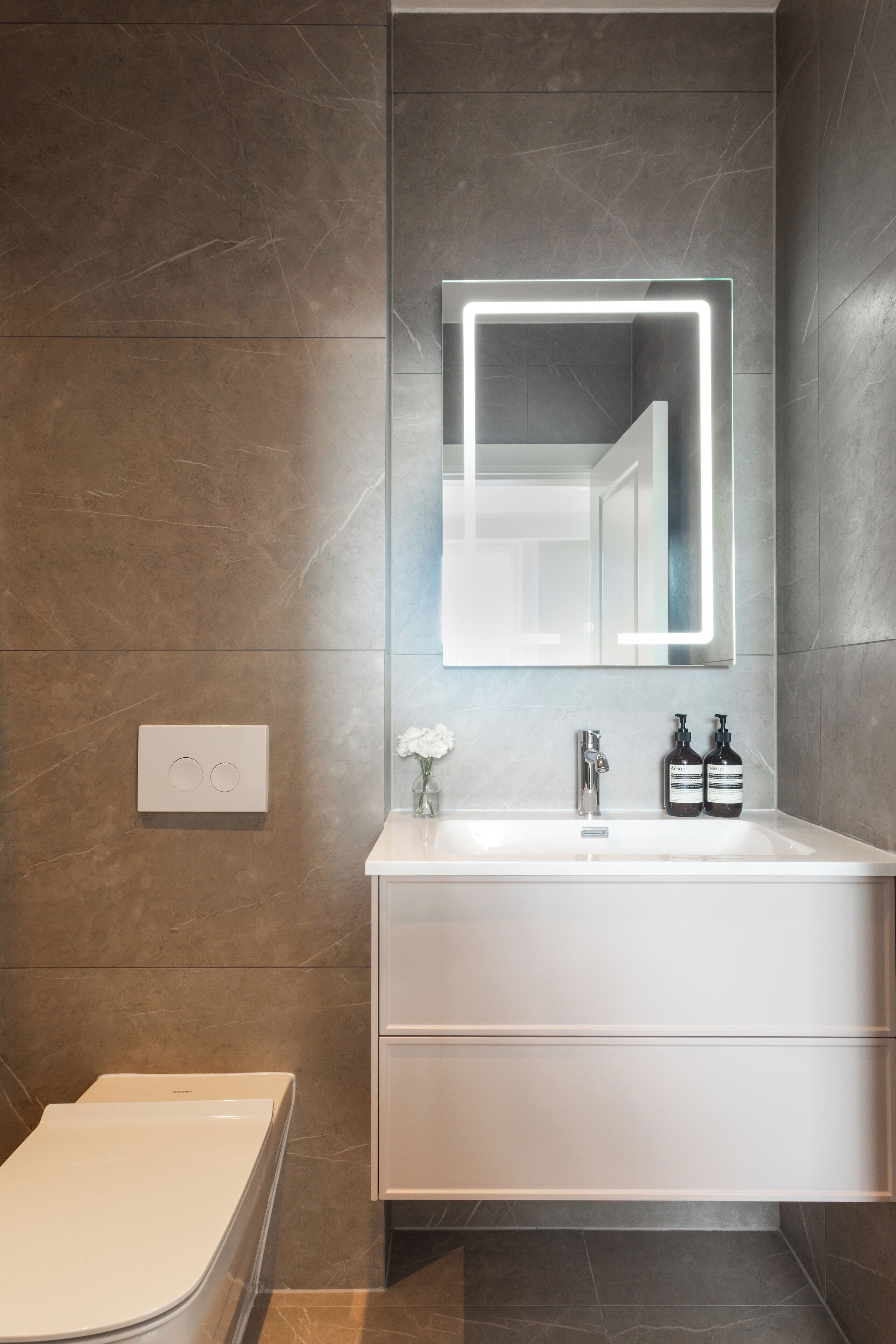 Ein modernes Badezimmer mit einem weißen Waschtisch, einem großen Spiegel mit Neonbeleuchtung und einer Toilette.