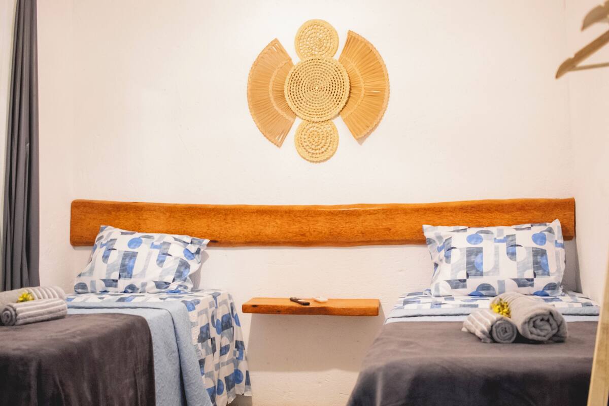 Habitación de hotel con dos camas, cada una con una colcha de diseño azul y blanco, cabeceros de madera y un adorno decorativo en la pared.