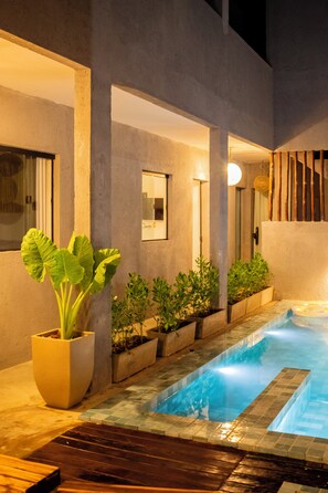 Een modern buitenzwembad met een jacuzzi, omgeven door potplanten en een houten terras.