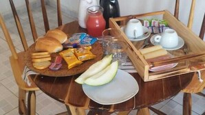 A wooden dining table with a tray of food, including bread, cheese, and fruit, and a coffee pot. - Vila Malie Milagres (São Miguel dos Milagres)