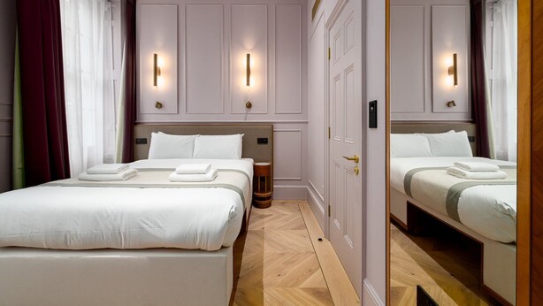 Een hotelkamer met twee bedden, een houten vloer en een spiegel die de kamer weerspiegelt.