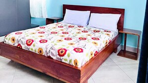 A bedroom with a wooden bed, a nightstand, a wall-mounted lamp, and a large window with curtains. - Apartment unit-Pearl Residence (Kampala)