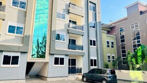 A multi-story residential building with balconies, a car parked in front, and a clear sky. - Apartment unit-Pearl Residence (Kampala)