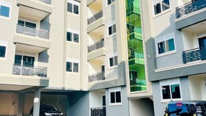 A multi-story residential building with balconies, a covered parking area, and a distinctive green facade. - Apartment unit-Pearl Residence (Kampala)