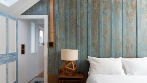 Un dormitorio con cama, una mesita de noche de madera con lámpara y una pared rústica de tablones verticales.