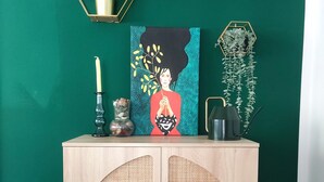 A wooden cabinet with woven doors, a painting, a candle, and two hexagonal wall decorations with plants.