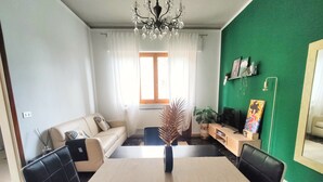 A dining area with a black table and chairs, a sofa, a TV, and a green accent wall.