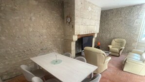 A room with a white table and four chairs, a stone fireplace, and beige sofas. - House Air conditioning in the countryside Vouvray (Vouvray)