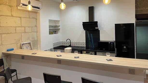 A modern kitchen with a bar area, featuring a black stove, a black refrigerator, and a wooden counter with bar stools. - House Air conditioning in the countryside Vouvray (Vouvray)