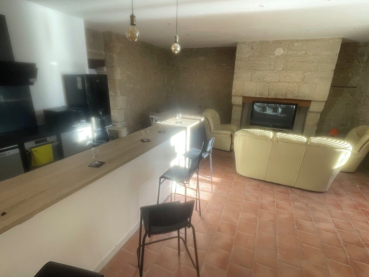 Una cuina moderna amb una illa central, tamborets de bar i una llar de pedra.