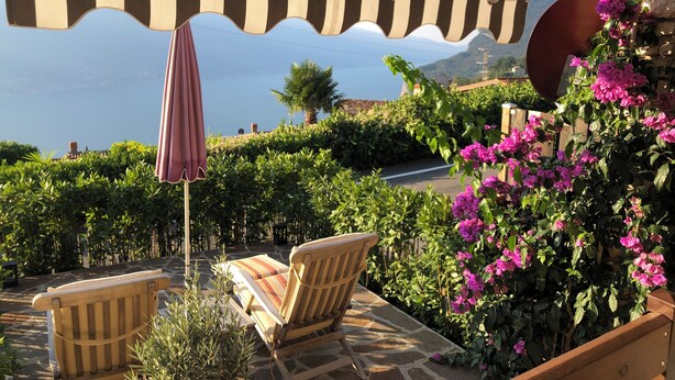 A patio with striped awning, outdoor seating, and a view of the sea.