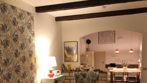 A living room with a sofa, armchair, and coffee table, a kitchen in the background, and a dining area with chairs.