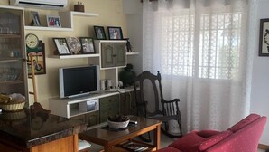 Una sala de estar con un sofá rojo, una mesa de centro de madera, un televisor y un mueble con cuadros enmarcados.