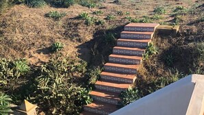 Un conjunto de escalones de piedra al aire libre que conducen a una zona de playa con vegetación escasa y una vista despejada del océano.