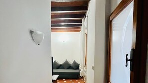 A narrow hallway with a tiled floor, a white wall with a light fixture, a wooden door, and a view into a room with a sofa and pillows. - Best Guelfa Affittacamere (Florence)