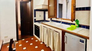A compact kitchen with a tiled floor, a small refrigerator, a sink, and a stove. - Best Guelfa Affittacamere (Florence)