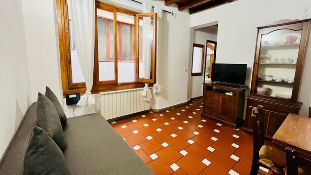 A living room with a sofa, a television, a wooden cabinet, and a patterned floor. - Best Guelfa Affittacamere (Florence)
