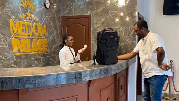 A reception desk with a marble wall, a clock, and a sign reading "MEDOM PALACE". - Résidence hôtelière MEDOM Palace, Bastos (Yaoundé)