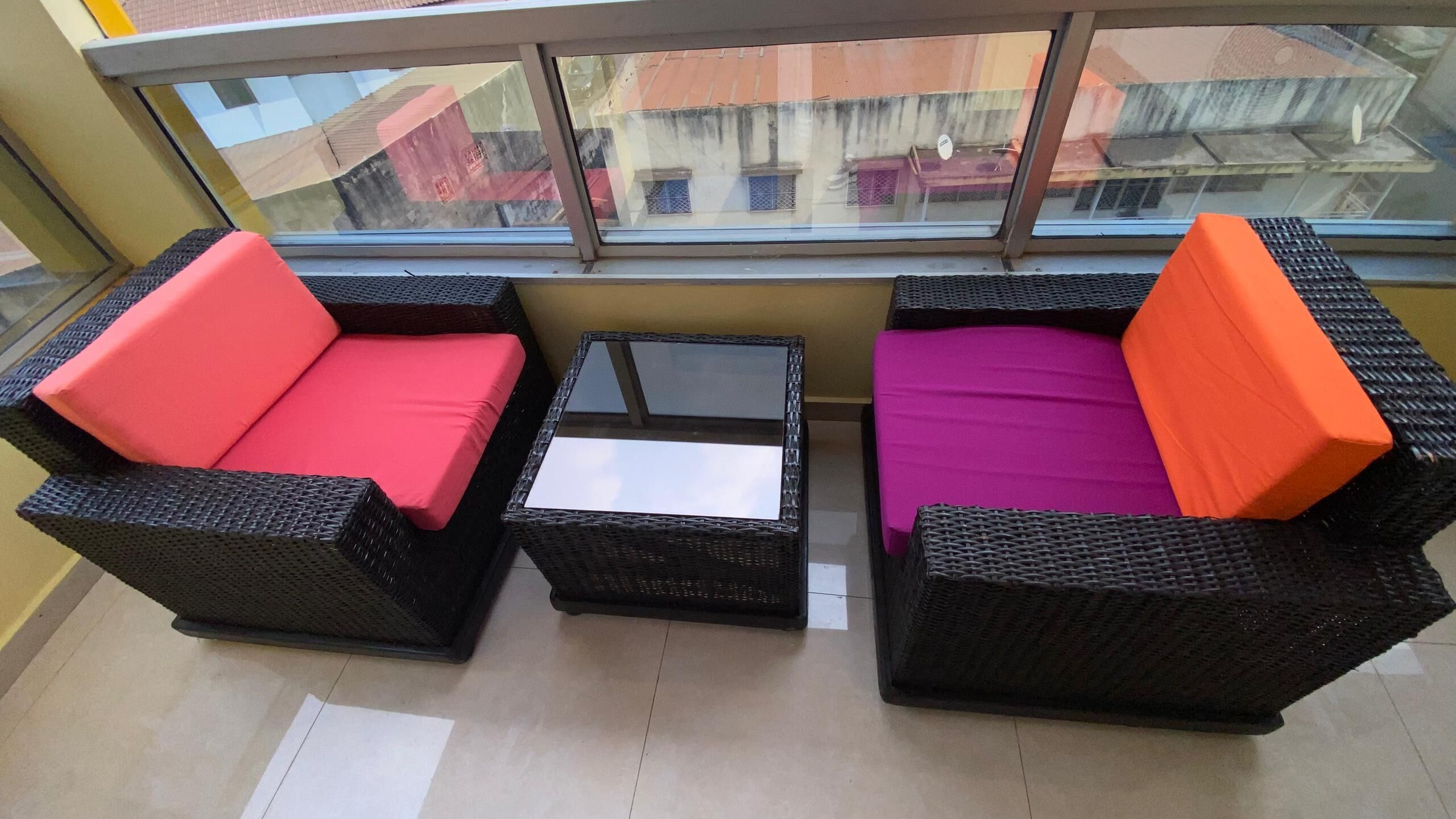 A balcony with wicker furniture, a glass table, and a view of buildings.