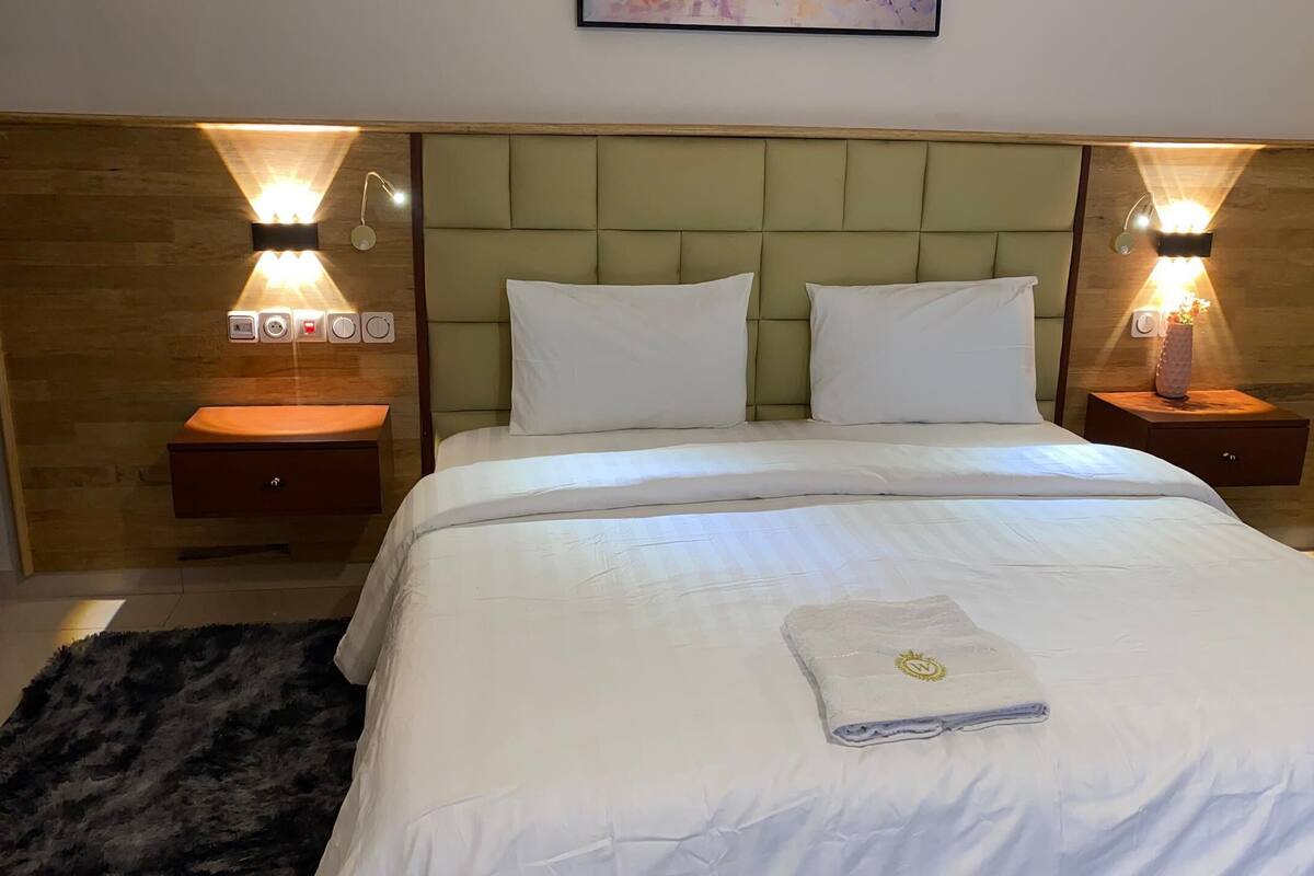 Hotellihuone, jossa on suuri sänky, kaksi yöpöytää, sängynpääty ja seinään kiinnitetyt valaisimet.