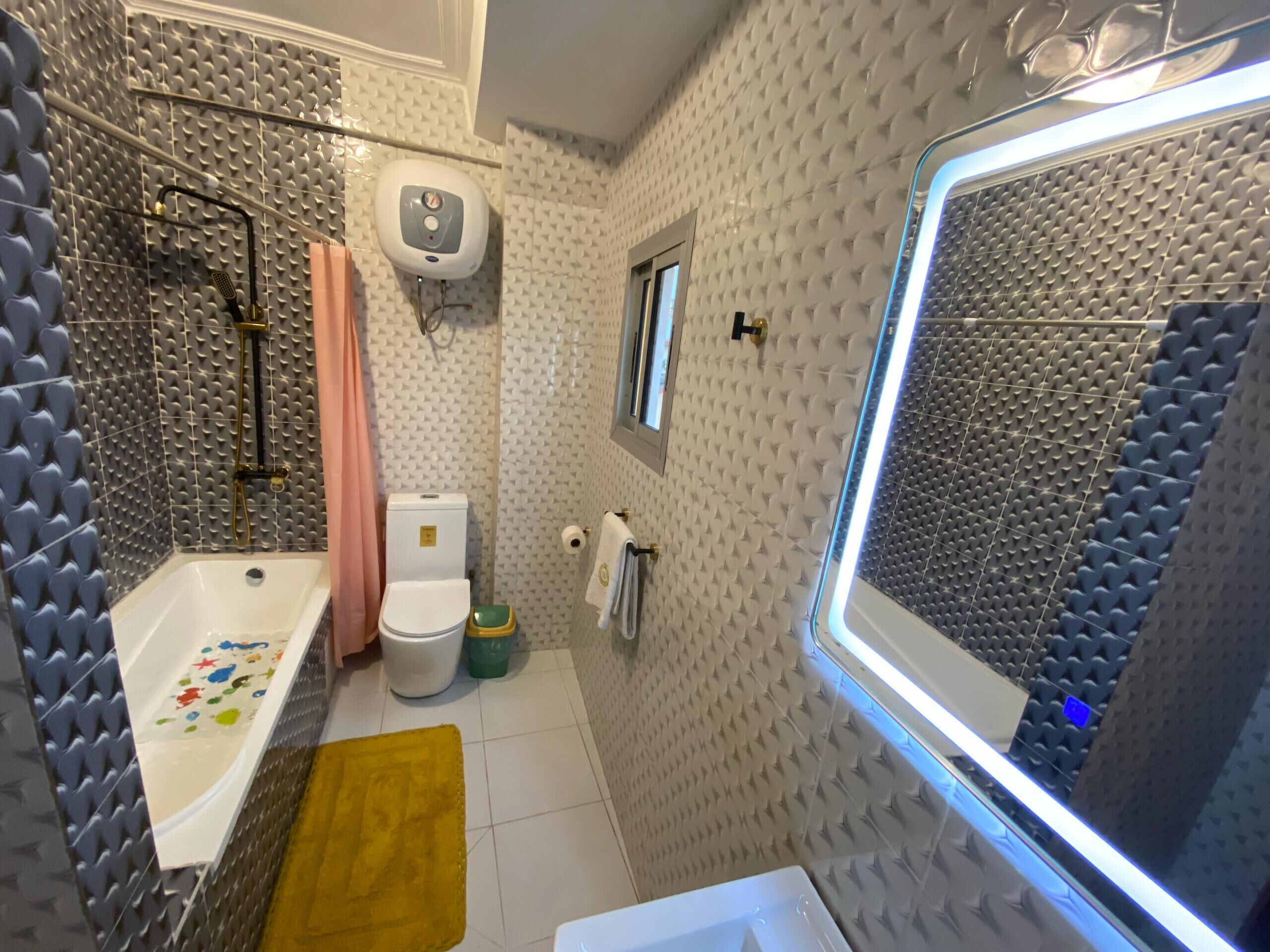 A bathroom with a bathtub, toilet, and shower area, featuring textured walls and a window with a view.