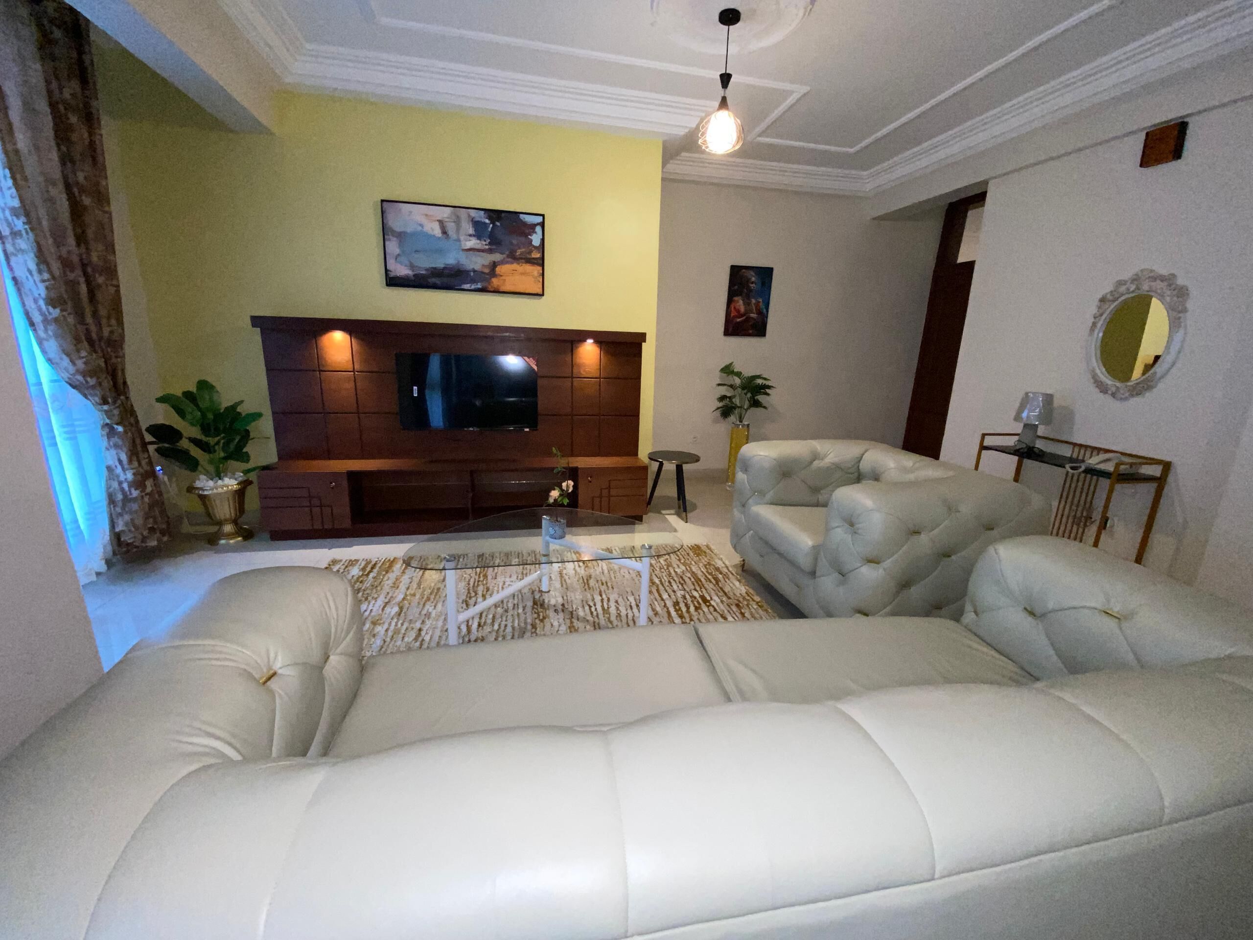 A living room with a large L-shaped sectional sofa, a flat-screen TV on a wooden entertainment unit, and a decorative mirror on the wall.