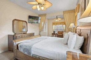 Een slaapkamer met een groot bed, een dressoir, een spiegel, een plafondventilator en een raam met gordijnen.