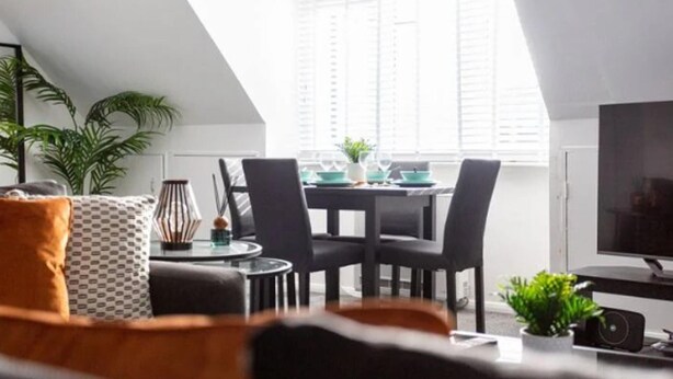 A modern loft apartment with a dining area, a TV, and a large window. - Loft Living Leigh-on-sea (Leigh-on-Sea)