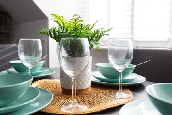 A dining table with a woven placemat, a potted plant, and teal-colored dinnerware.