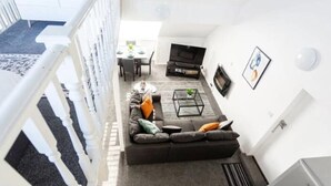 A modern living room with a sofa, coffee table, and TV. A staircase leads to an upper level. - Loft Living Leigh-on-sea (Leigh-on-Sea)